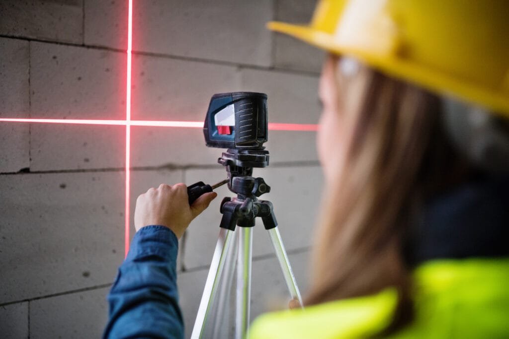 Female worker on the building site with line laser level. House construction.